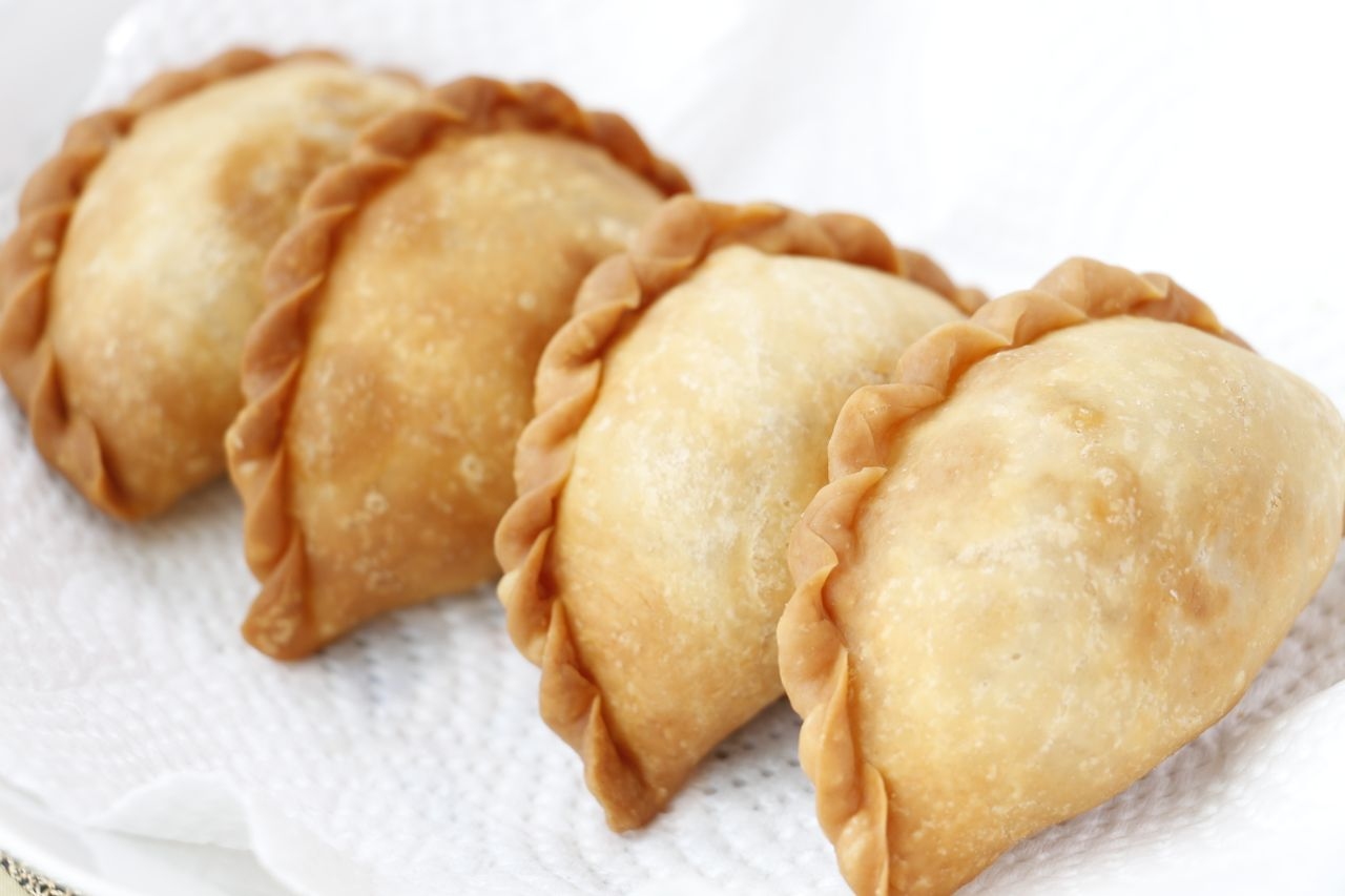 Four Malaysian curry puffs on a white plate.
