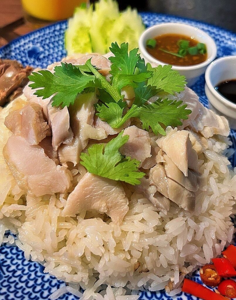 A closeup of chicken rice on a blue plate with a pair of sauces in the background.