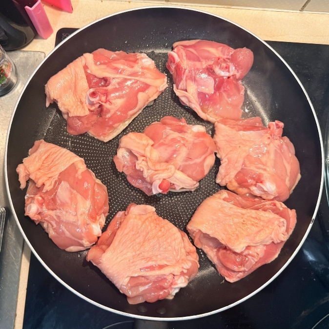 Raw bone-in chicken thighs arranged in a skillet.