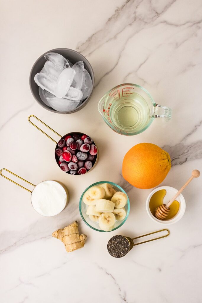 cranberries, orange, banana and smoothie ingredients arranged on a marble counter