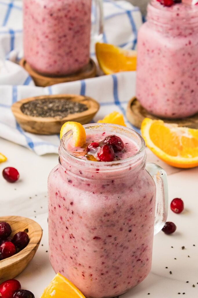 three pink smoothies with striped straws and orange wedges