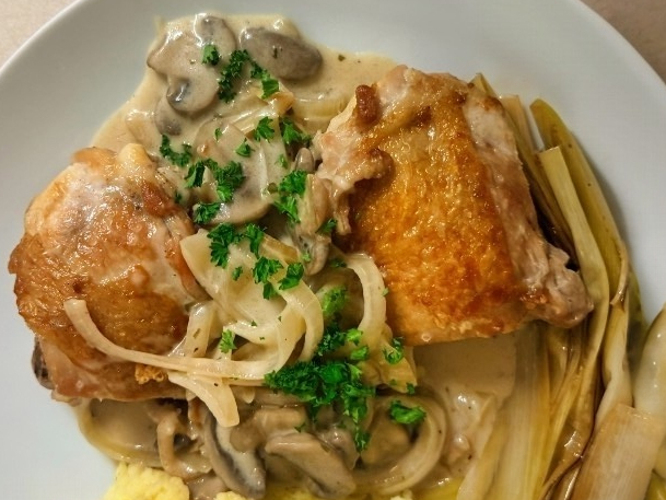 Golden chicken thighs with mushroom and onion sauce, chopped parsley and braised leeks.