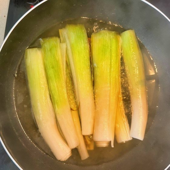 Leeks simmering in bubbling braising liquid.