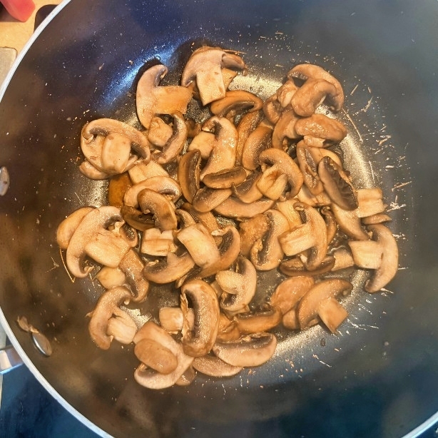 Sautéed mushroom slices with browned edges in a skillet.