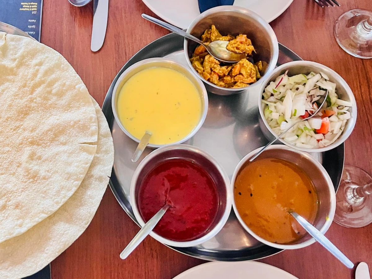 Poppadoms with bowls of chutneys, sauces and chopped onion salad on a restaurant table.