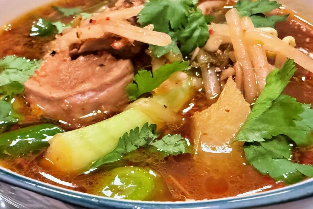 Close-up of pork, pineapple and greens in Cambodian sour soup topped with cilantro.
