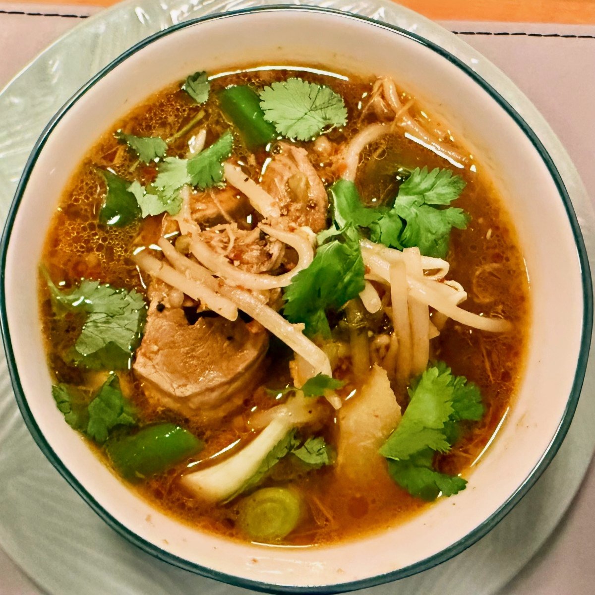 Overhead view of Cambodian pork soup with bean sprouts, greens and cilantro.