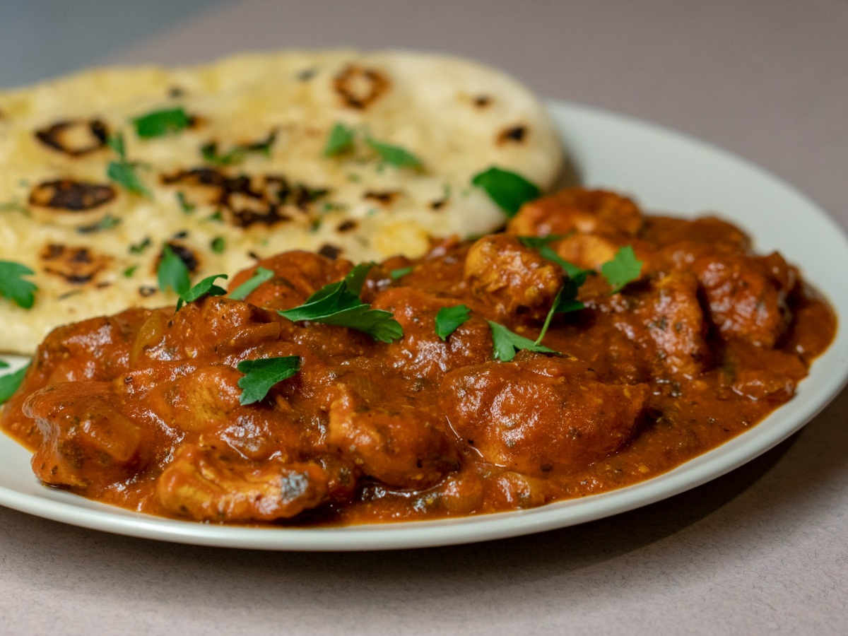 Chicken tikka masala with fresh herbs and naan on a white plate. Well-known British Indian food.