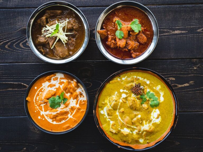 Four dishes of curry with cream and herb garnishes on a dark wooden table.