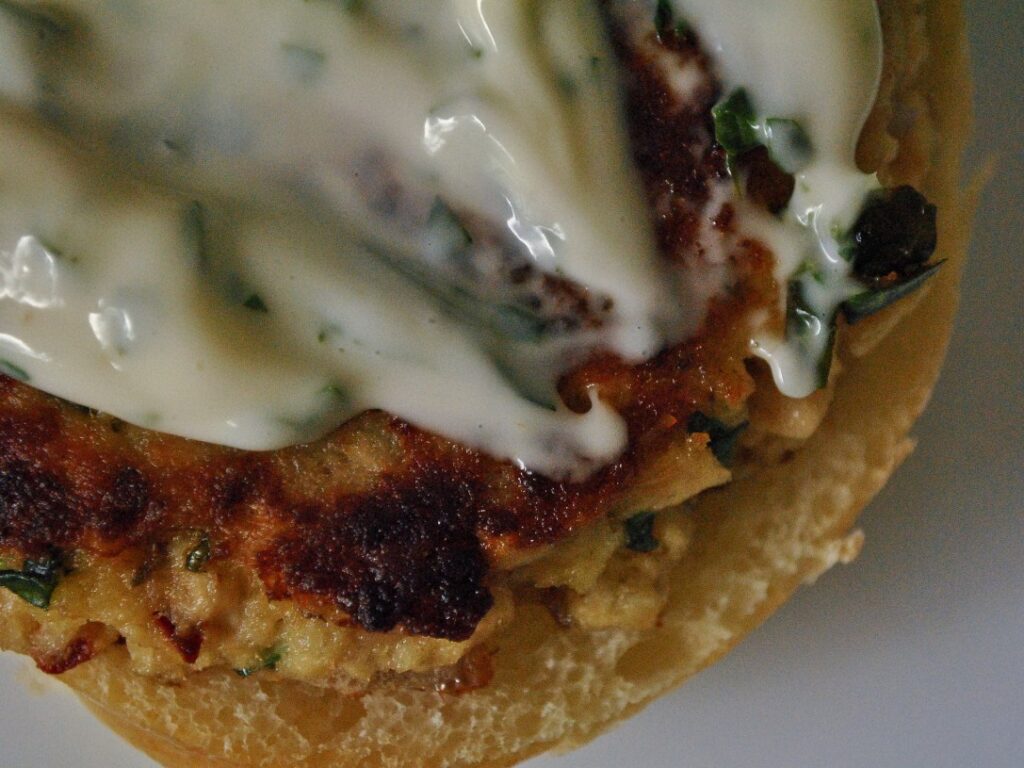 Salmon patty topped with white herb sauce, viewed from above on an open bread roll