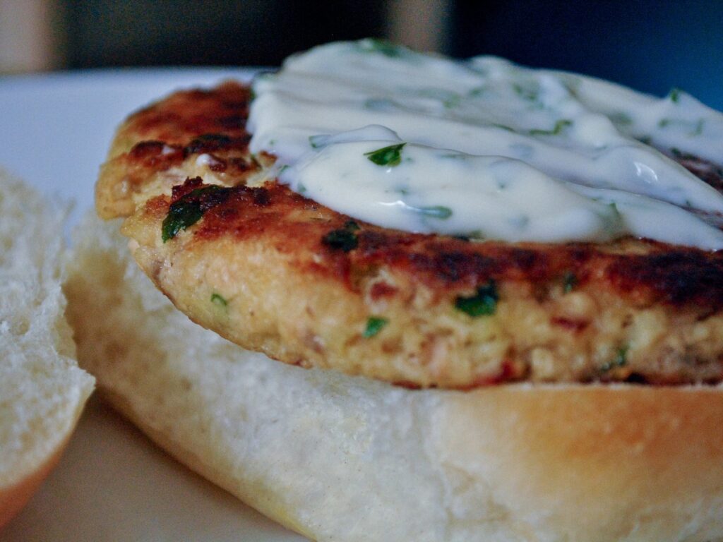 Browned salmon patty topped with white herb sauce on an open bread roll