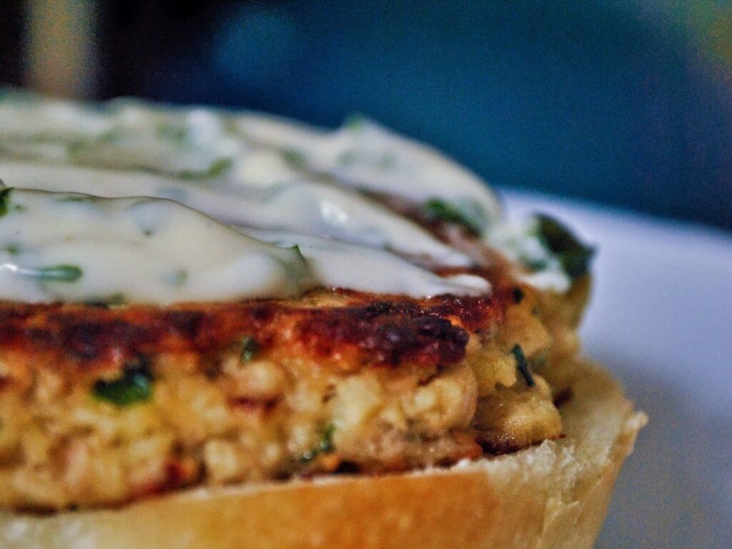 Close-up of a browned salmon patty with white sauce on a bread roll