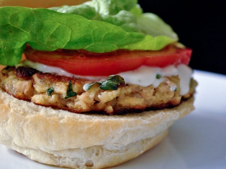 Salmon patty sandwich with lettuce, tomato and white sauce on a bread roll