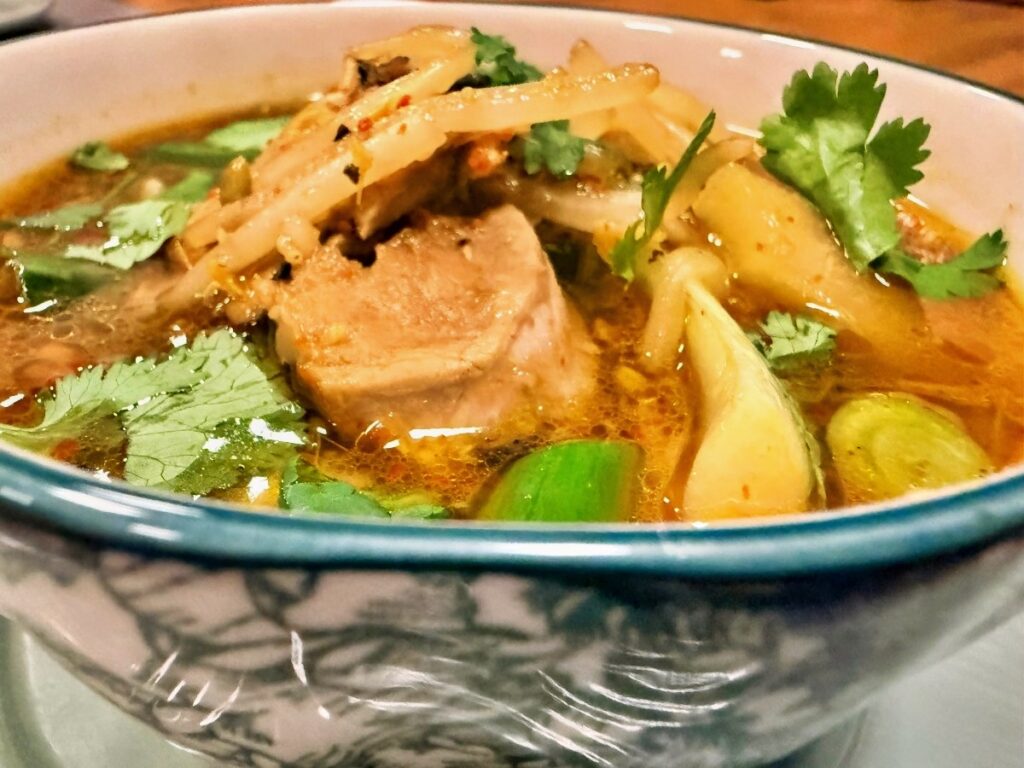 Pork and bean sprouts in sour soup with pineapple and cilantro.