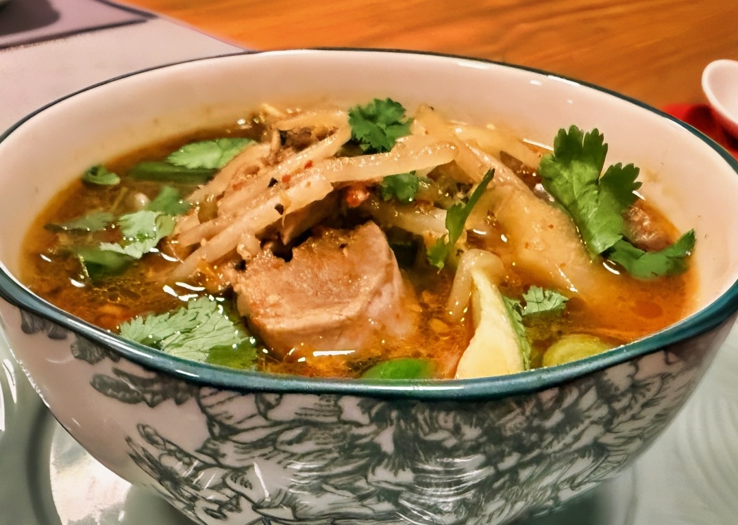 Cambodian sour soup with pork, pineapple, bean sprouts and cilantro in a patterned bowl.